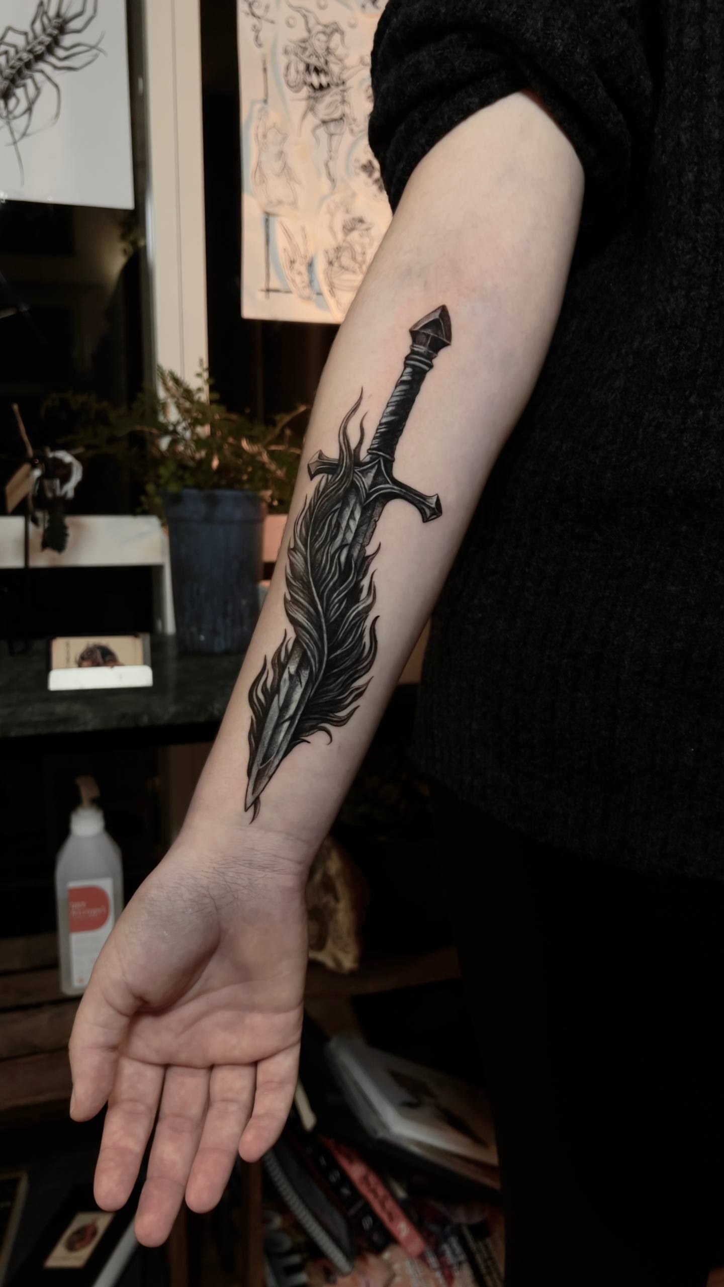 Dark fantasy tattoo Uppsala — sword and feather in blackwork, forearm