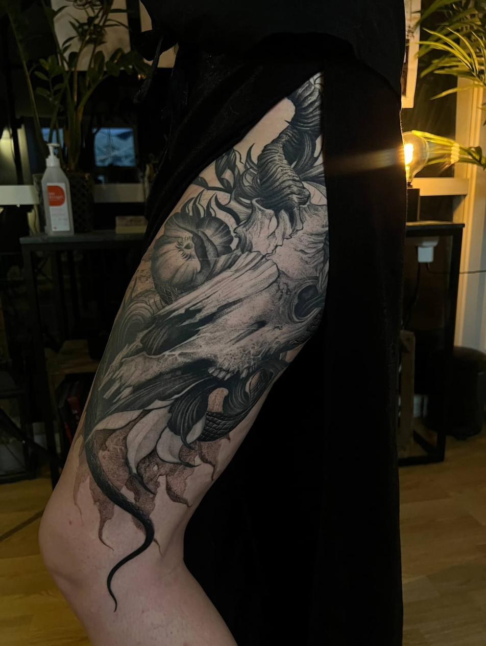 Dark fantasy tattoo artist Uppsala — skull with snake and flowers, thigh